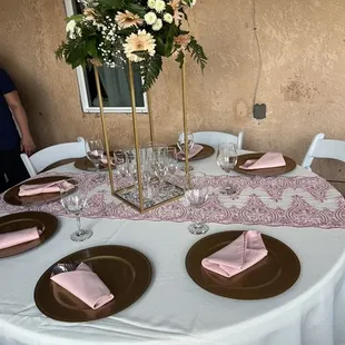 Tables, chairs, chair covers, tablecloths, table overlays, floral arrangement, plates, silverware, center piece, patio chair
