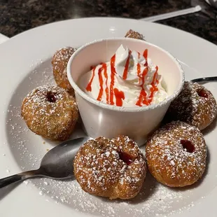 a bowl of powdered sugared doughnuts and a bowl of whipped cream