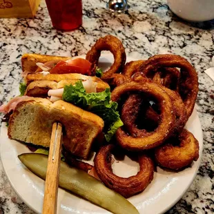 a plate of food with onion rings and a pickle