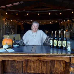 a woman behind a table with bottles of wine
