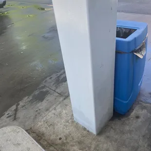 a blue trash can next to a white pillar
