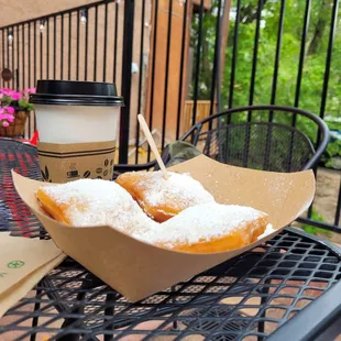 a cup of coffee and a basket of powdered sugared doughnuts