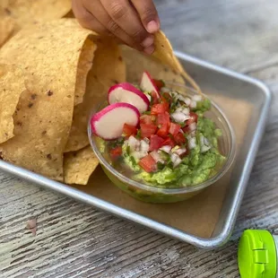 a person dipping a tortilla into a bowl of guacamole