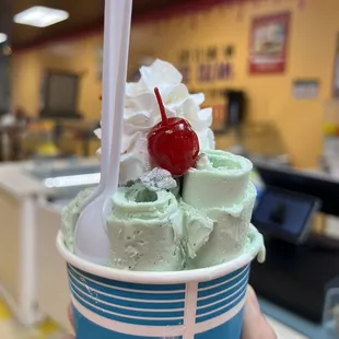 a hand holding a cup of ice cream with a cherry on top