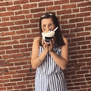 a woman holding a cup of ice cream in front of a brick wall