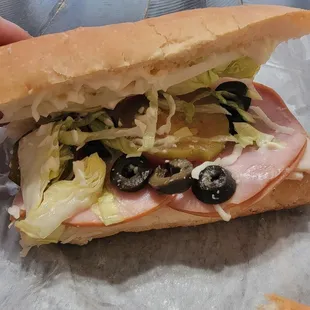 a sub sandwich with meat, lettuce, and olives
