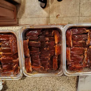 three pans of ribs on a counter