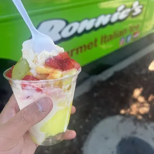 Medium Pineapple Ice and Vanilla custard gelati with strawberry and pineapple chunk toppings along with a grape and a lime