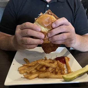 a man eating a chicken sandwich and french fries