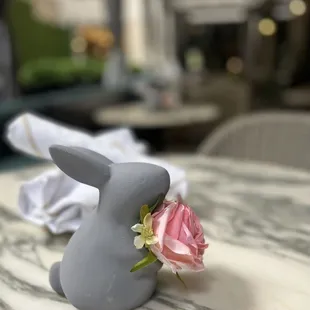 a grey rabbit with a pink rose in its mouth