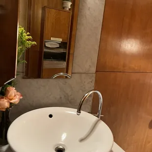 Restroom showing cute sink and a small bouquet of orange roses in the corner