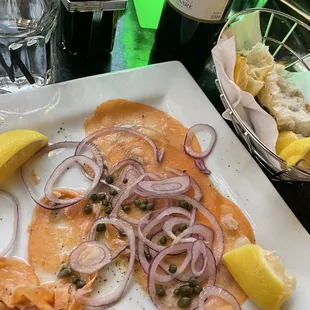 Salmon carpaccio with lemon, capers, onions, and warm bread