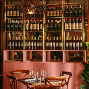a table and chairs in front of a wall of wine bottles