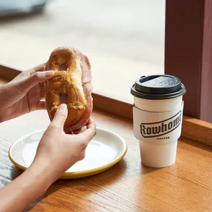 a person holding a donut and a cup of coffee