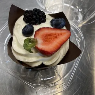 a cupcake with whipped cream, strawberries, and blueberries