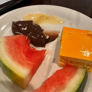 Half eaten water melon, half eaten snack pack jellos, orange fluffy cake.
