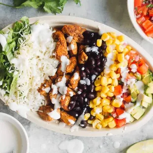 a bowl of chicken, rice, corn, black beans, avocado, corn, cilantro sauce,