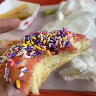 a hand holding a donut with sprinkles