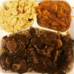 Succulent fall off the bone oxtail platter over a bed of rice and peas with sweet candied yams and baked macaroni and cheese