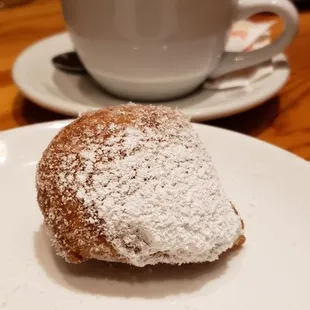 a powdered donut on a plate with a cup of coffee