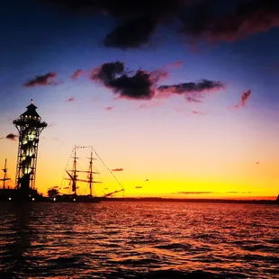 a tall ship in the water at sunset