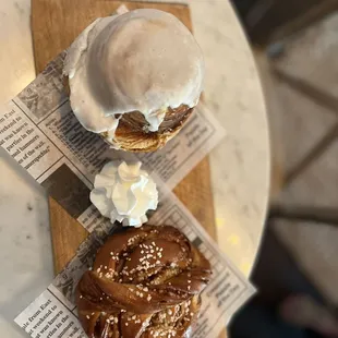 The cinnamon bun and the cinnamon roll with a side of wiped crème. (Cinnamon bun is on bottom and cinnamon bun is on top)