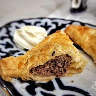 Meat Pirozhki - Baked pies made with filo dough, stuffed with ground beef and onions seasoned with spices, served with sour cream.