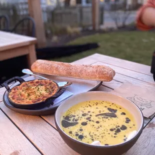 a bowl of soup and a pan of bread on a picnic table