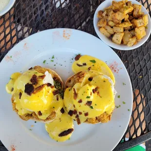 a plate of eggs benedict and potatoes