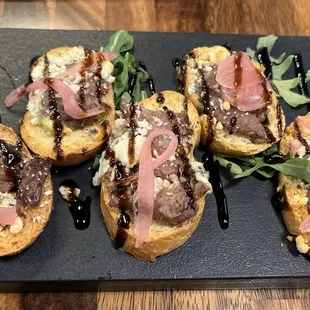 BLACK &amp; BLUE: shaved prime rib, garlic cilantro, blue cheese, pickled onion, balsamic glaze, on toasted crostinis