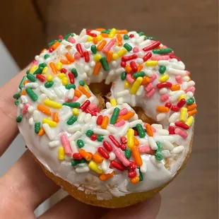 a hand holding a frosted donut with sprinkles