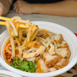 a close up of a bowl of noodles with chicken and vegetables