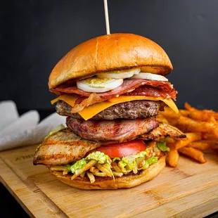 a burger with bacon, cheese, tomato, lettuce, and french fries