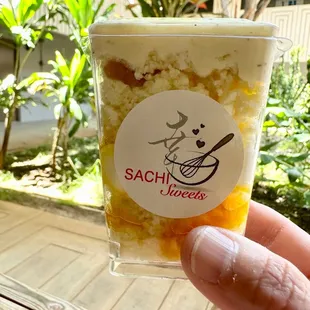 a hand holding a cup of sachi sweets