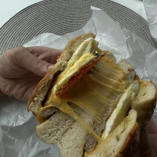 Cheese pull, breakfast bagel with sausage, bacon, and cheddar.