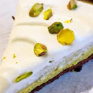 a slice of cake with white icing and pistachios