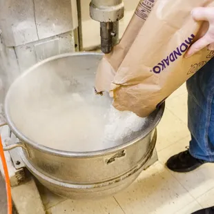 a person pouring a bag of dough into a large metal pot