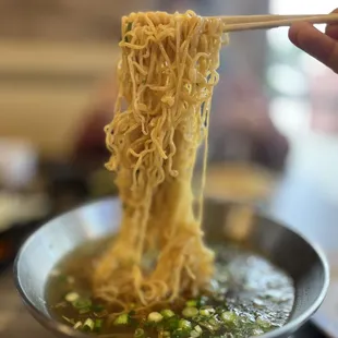 a person holding chopsticks over a bowl of noodles
