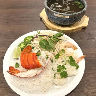 a plate of noodles, shrimp, and a bowl of soup