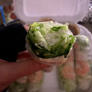 a hand holding a roll filled with lettuce and shrimp