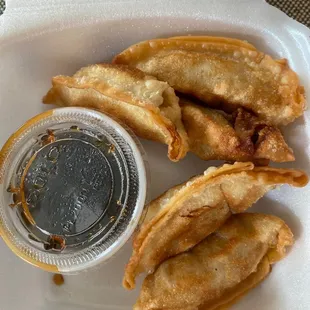 a close up of a fried dumpling and a small sauce in a styrofoam container