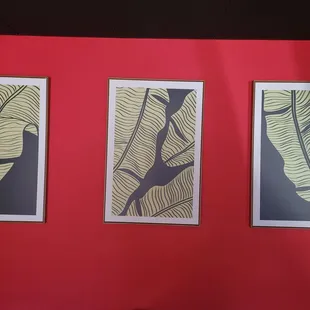 a red wall with three paintings of banana leaves