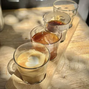 A four drink flight containing a latte, iced single origin, hot single origin, and a shot of espresso.
