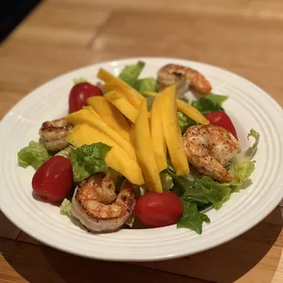 a plate of salad with shrimp and mangoes