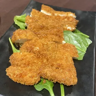 two pieces of fried chicken on a black plate
