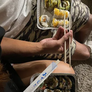 a person holding a tray of sushi and chopsticks