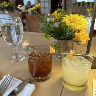 a table with a vase of flowers and a drink