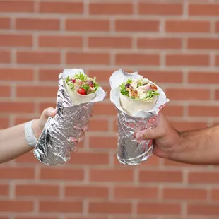 two people holding wraps in front of a brick wall