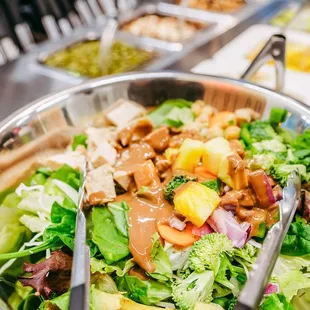 a salad in a metal bowl with tongs