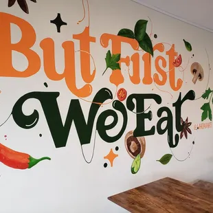 a wall with a sign that says but first we eat